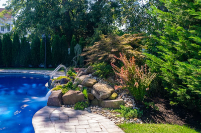 Tumalo C - Freehold, NJ - A backyard with a swimming pool surrounded by lush greenery and rocks