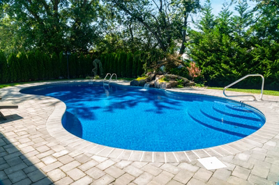 Tumalo H - Freehold, NJ - A rectangular swimming pool surrounded by lush greenery and trees.