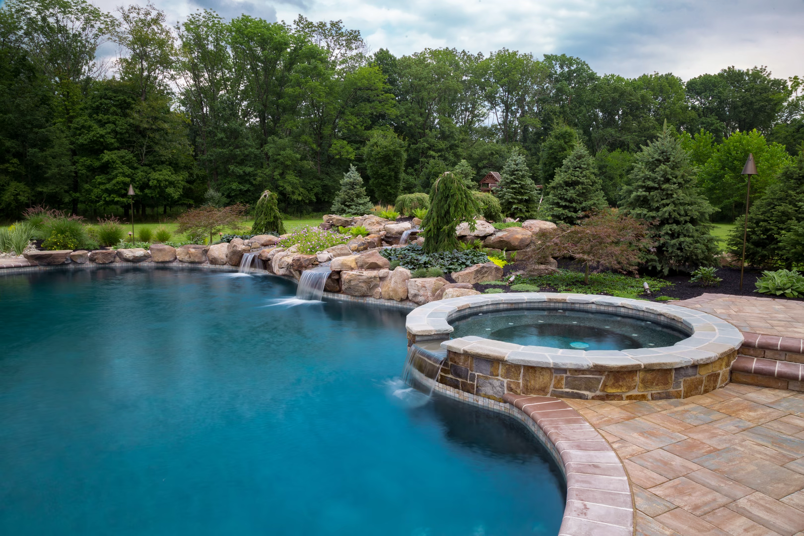 Natural stone boulder waterfalls cascade into a freeform pool surrounded by lush greenery
