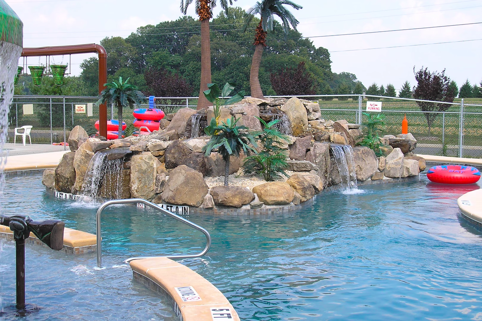 Natural stone boulder waterfalls cascading into a swimming pool with tropical palm trees