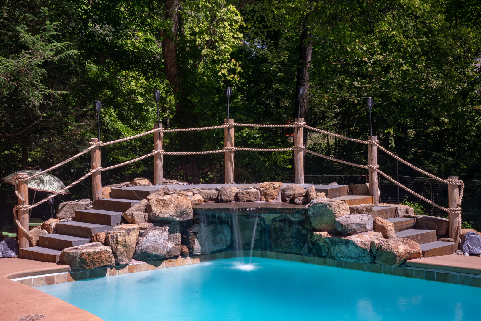 Natural stone boulder waterfall cascading into a pool surrounded by lush green trees