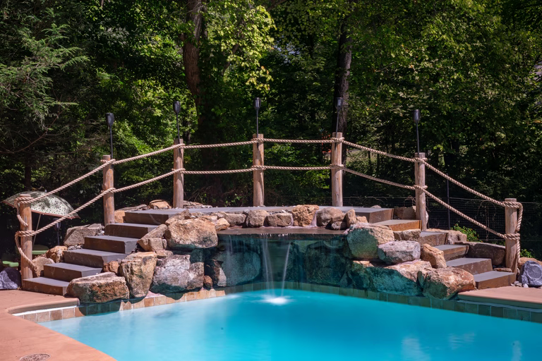 Natural stone boulder waterfall cascading into a pool surrounded by lush green trees