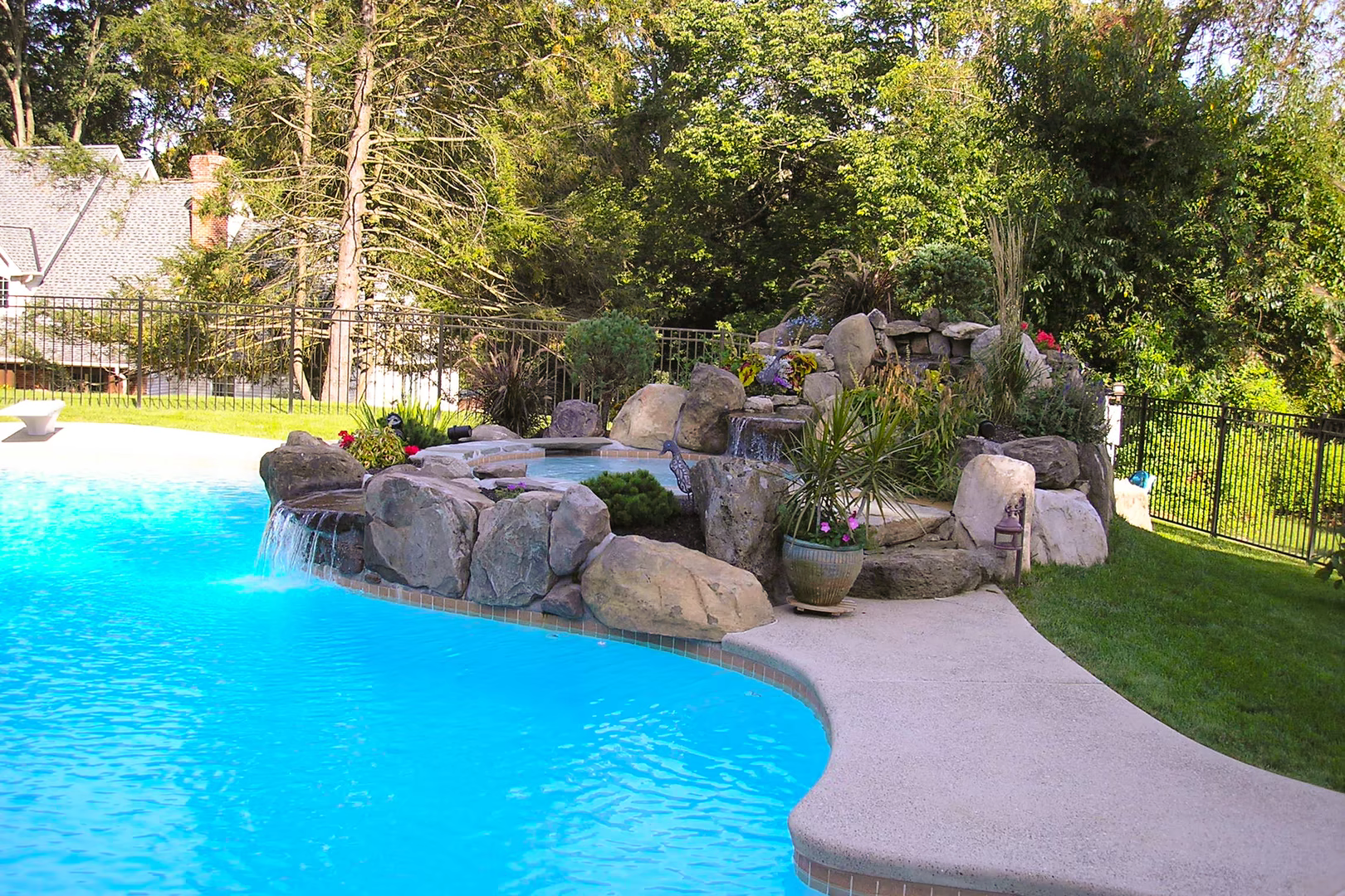 Natural stone boulder waterfall cascading into a pool surrounded by lush garden plants