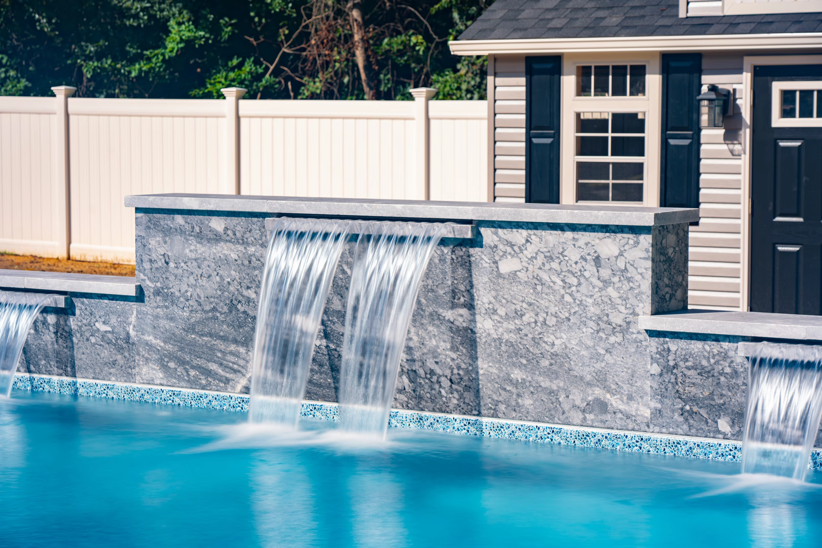 Natural stone wall with sheer descent waterfalls cascading into a pool near garden foliage