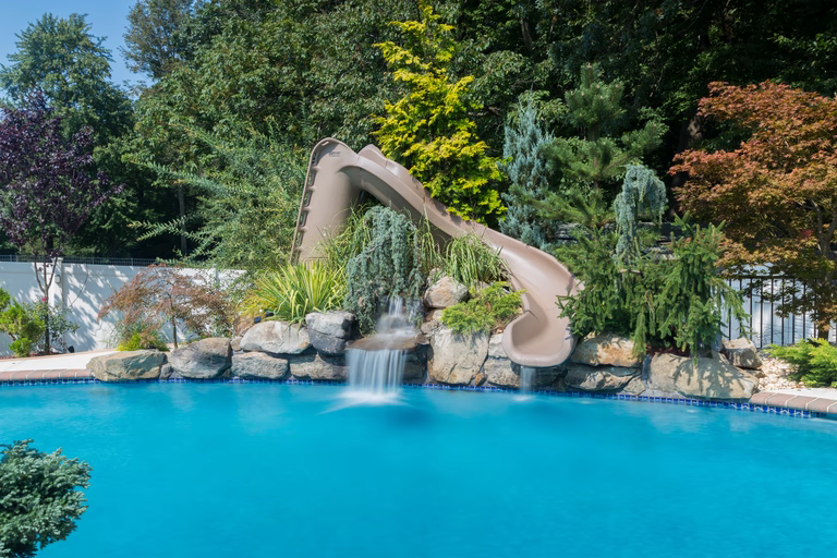 Natural stone boulder waterfall cascading into a pool surrounded by lush garden plants