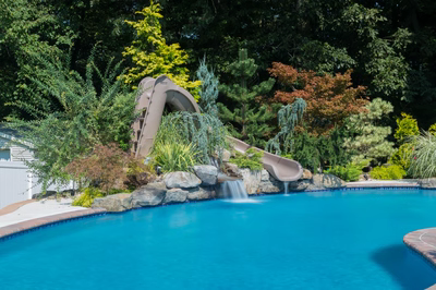 Wentworth B - Morganville, NJ - A swimming pool with a water feature and a slide surrounded by lush greenery