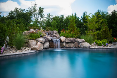 Willey C - Moorestown, NJ - A swimming pool with a waterfall surrounded by lush greenery and colorful flowers