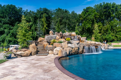 Yakso C - Mullica Hill, NJ - A large rock waterfall in the middle of a swimming pool surrounded by lush greenery
