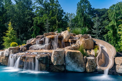 Yakso F - Mullica Hill, NJ - A large rock waterfall with a slide in the middle of a pool surrounded by lush greenery