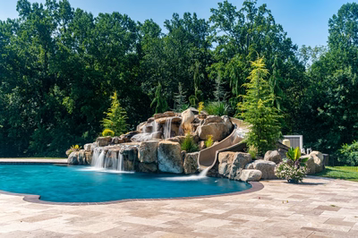 Yakso H - Mullica Hill, NJ - A swimming pool with a waterfall and a slide surrounded by lush greenery