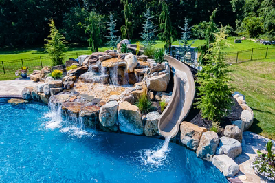 Yakso I - Mullica Hill, NJ - A swimming pool with a waterfall and a water slide surrounded by lush greenery