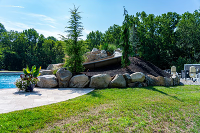 Yakso J - Mullica Hill, NJ - A large rock structure with a wooden canoe on top of it next to a swimming pool