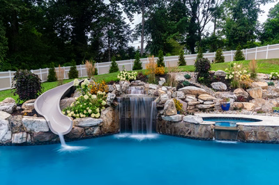 Yosemite E - Newtown Square, PA - A swimming pool with a waterfall and a slide surrounded by lush greenery