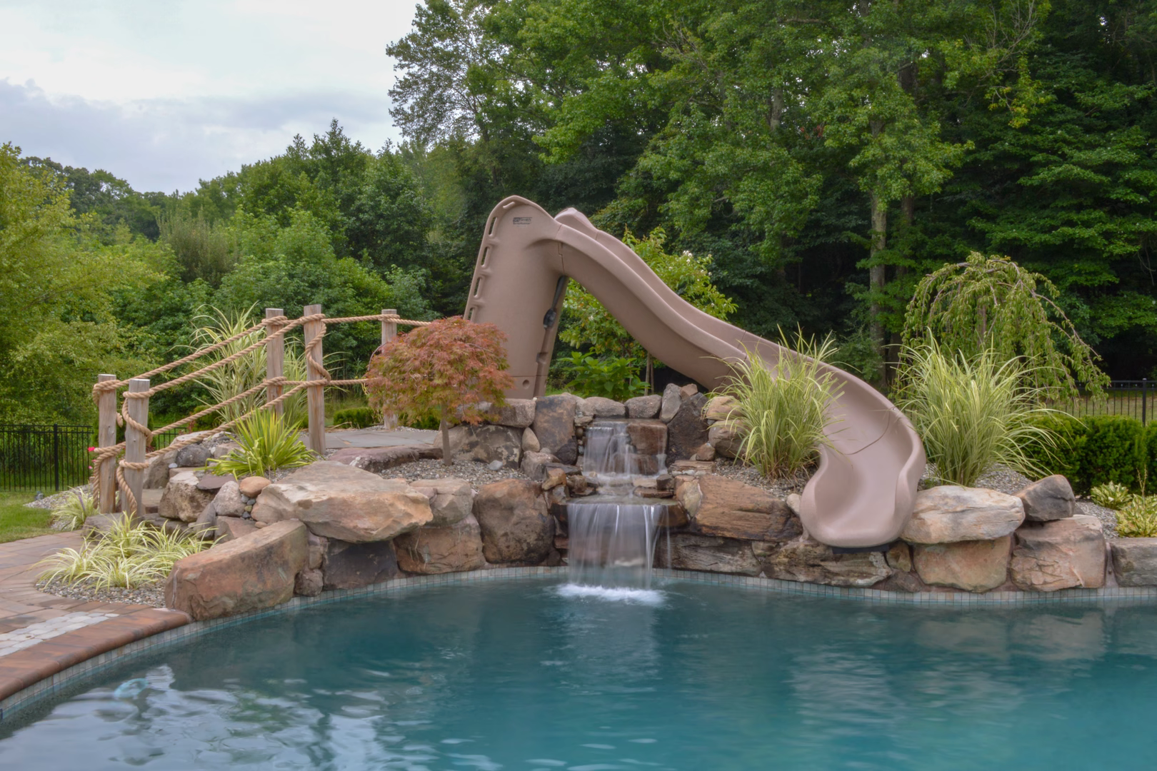 Natural stone boulder waterfall cascading into a pool surrounded by lush greenery and plants