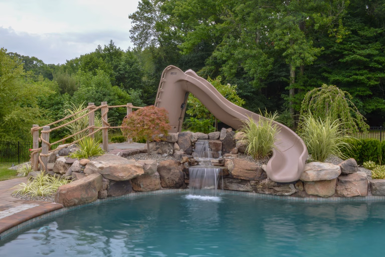 Natural stone boulder waterfall cascading into a pool surrounded by lush greenery and plants