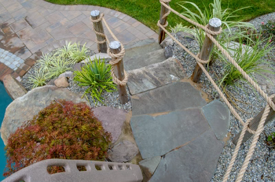 Zillie F - Manalapan, NJ - A stone path leading to a swimming pool surrounded by plants and rocks