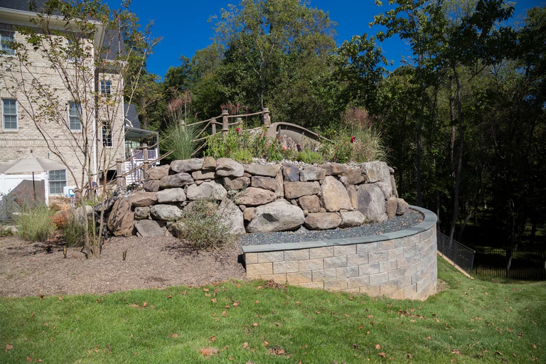 A large stone retaining wall in front of a large house