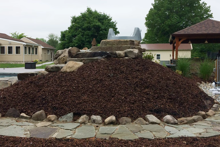 A large pile of mulch in front of a house with a gazebo in the background