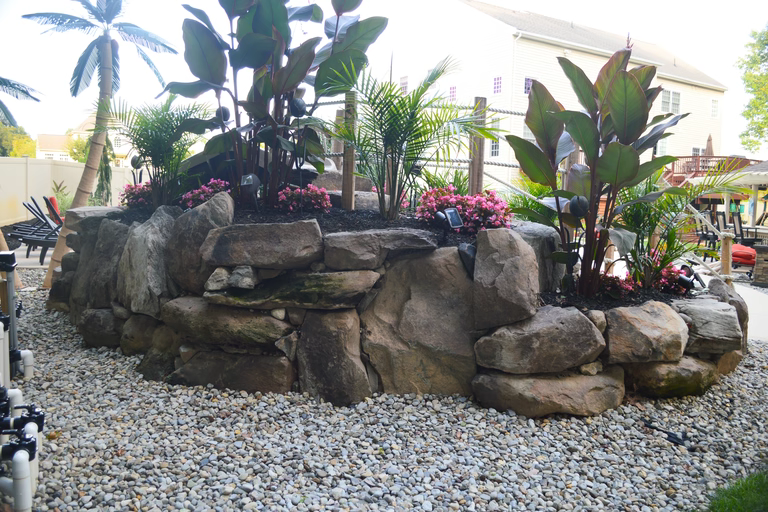 A rock retaining wall with plants and flowers in a backyard setting