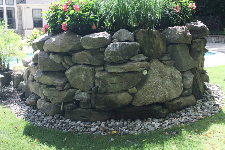 A stone retaining wall with flowers in it in a backyard setting