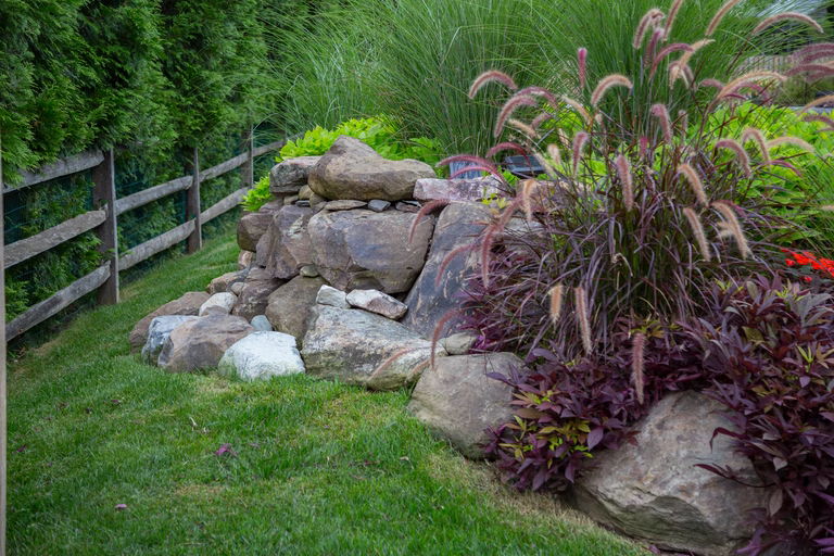 A rock wall in a grassy area with a wooden fence in the background