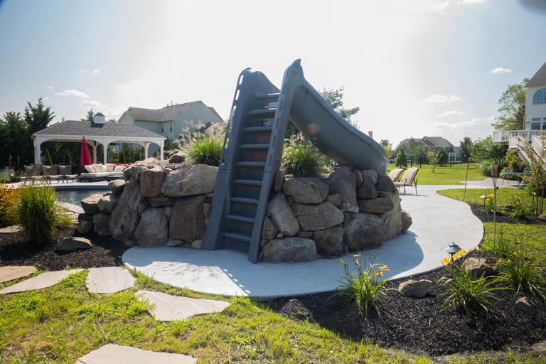 A backyard with a stone play structure and a slide in the middle of it