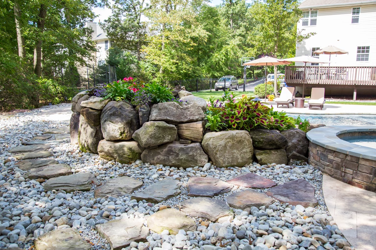 A stone retaining wall with flowers in it next to a swimming pool