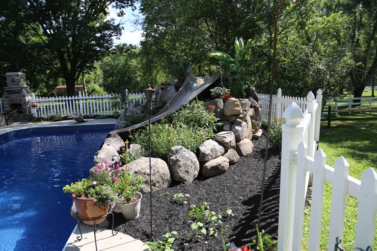 A backyard with a white picket fence and a rock wall with a water slide