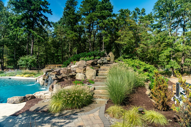 A landscaped area near a swimming pool with a waterfall and steps leading up to it