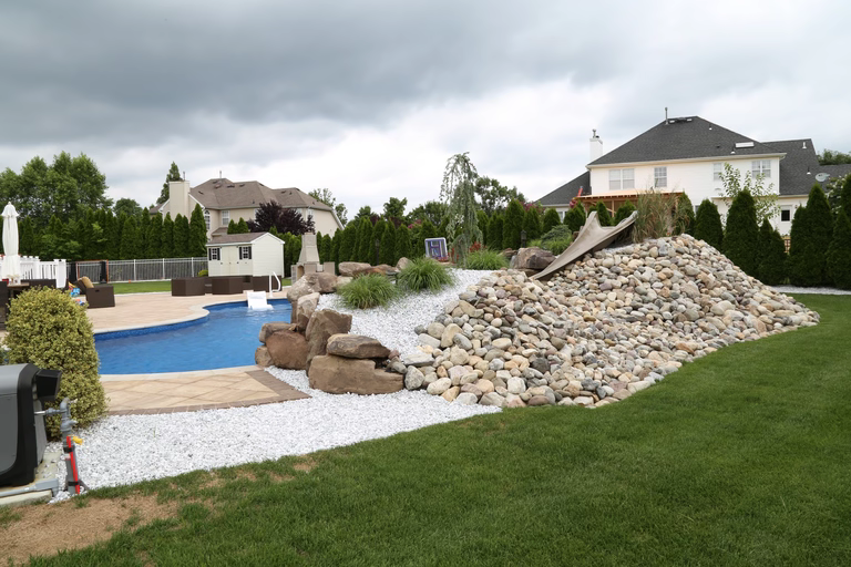A backyard with a large rock wall next to a swimming pool