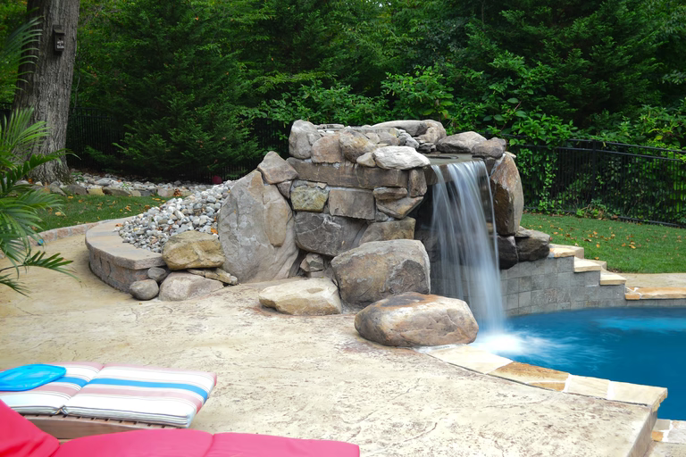 A pool with a waterfall in the middle of it surrounded by lush greenery