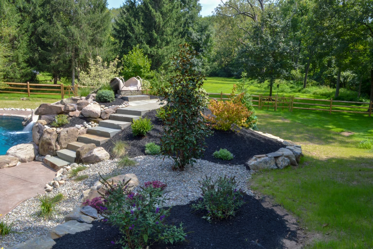 A backyard with a rock garden and a wooden fence surrounding a swimming pool