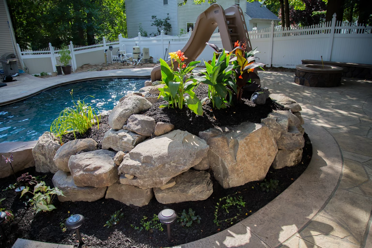 A rock garden with a water feature and a slide in a backyard setting
