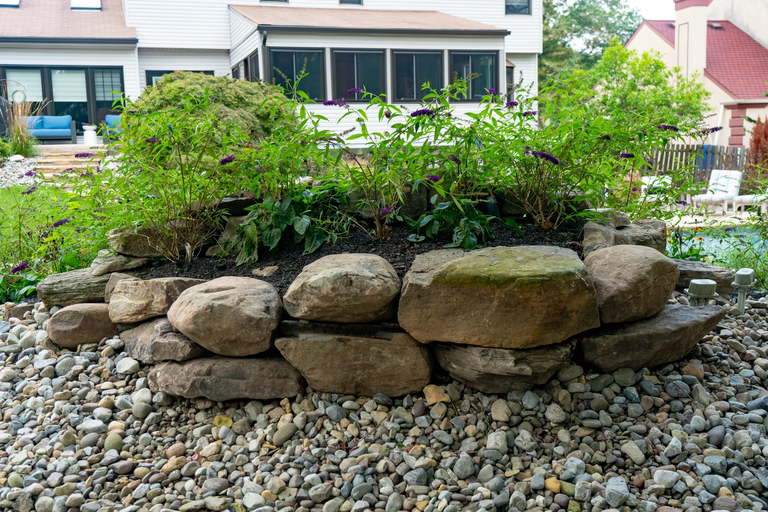 A rock garden in front of a white house with a pool in the background
