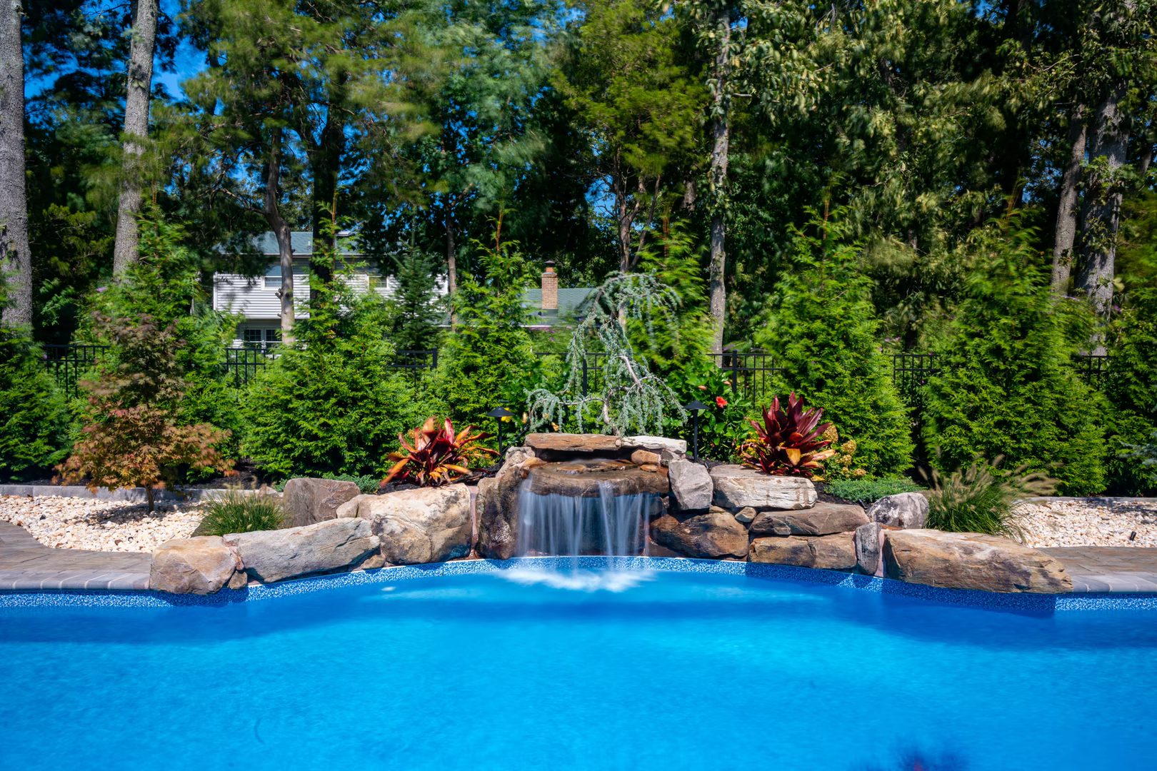 Two-tiered natural stone boulder waterfall cascading into a blue pool surrounded by lush greenery