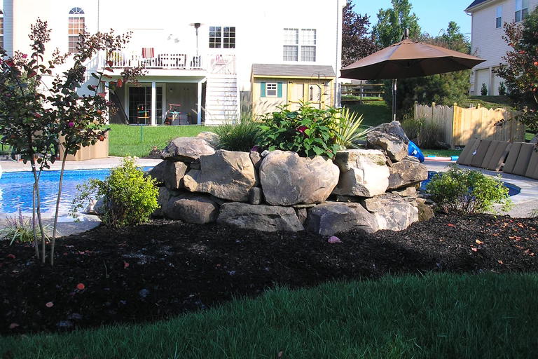 Natural stone boulder waterfall cascading into a pool surrounded by lush garden plants