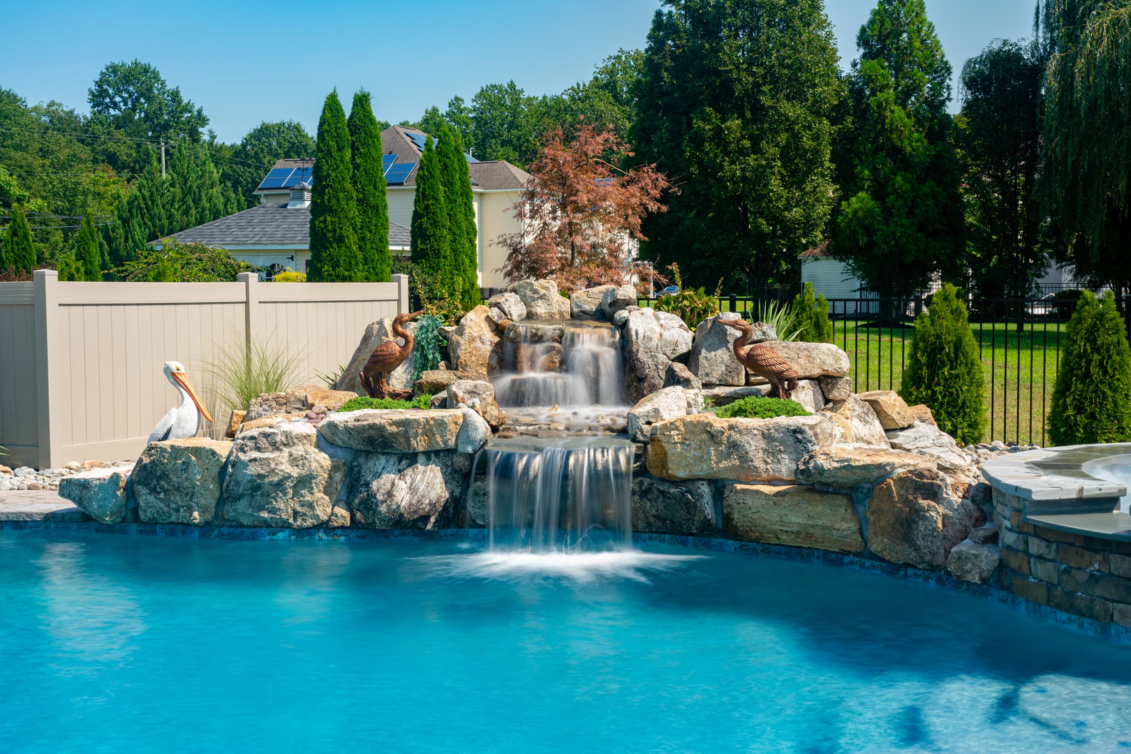 Natural stone boulder waterfall cascading into a pool with decorative statues and lush greenery