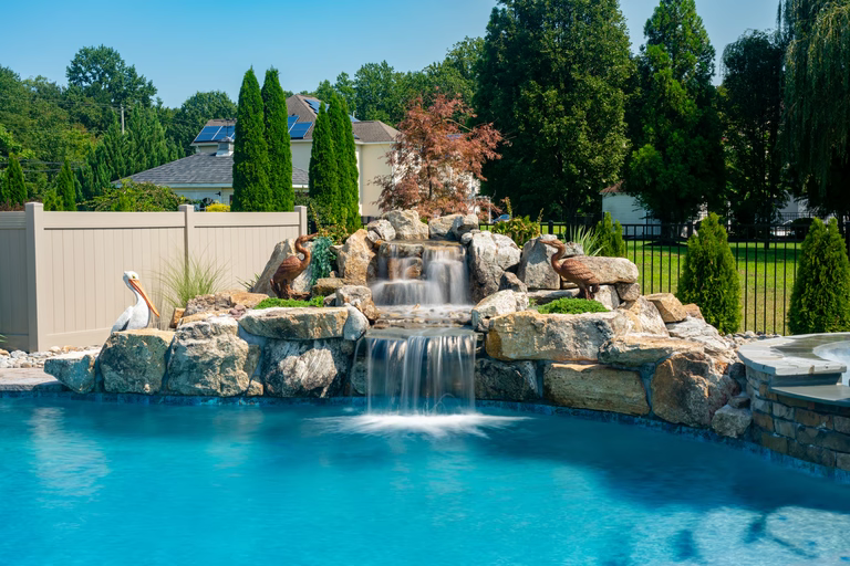 Natural stone boulder waterfall cascading into a pool with decorative statues and lush greenery