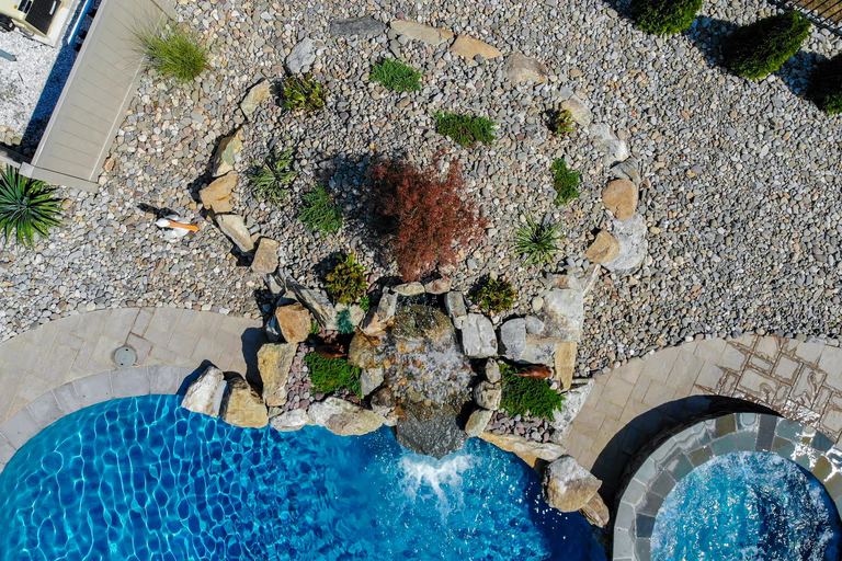 Natural stone boulder waterfall cascading into a pool surrounded by gravel and greenery