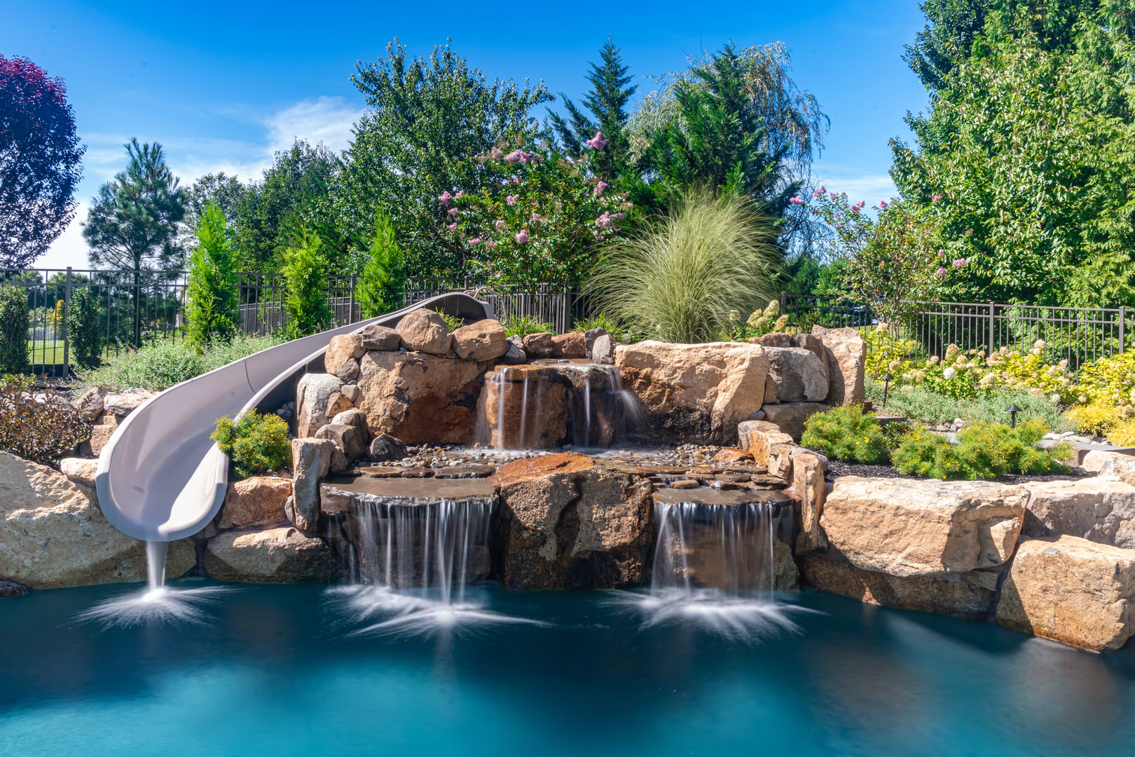 Three-tiered natural stone boulder waterfall cascading into a pool surrounded by lush garden greenery
