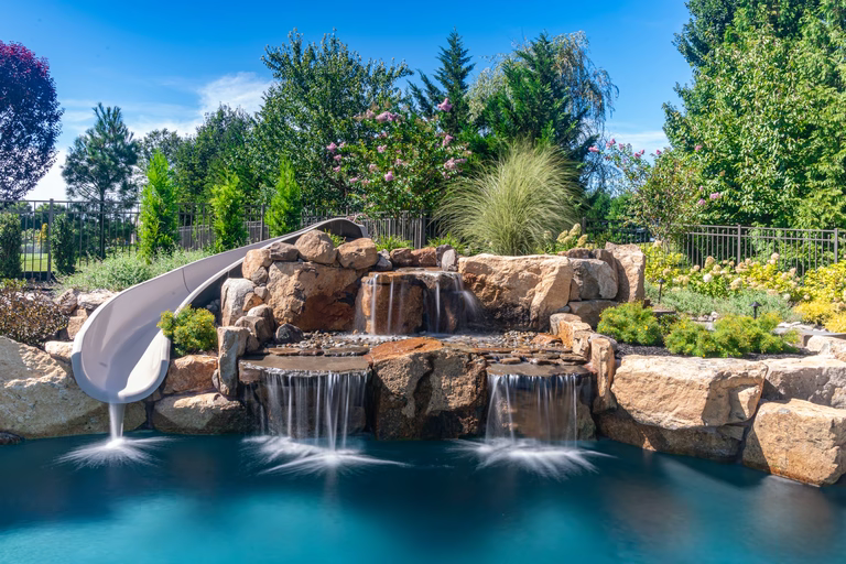 Natural stone boulder waterfall cascading into a pool surrounded by lush garden greenery