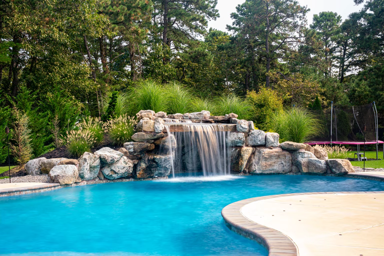 Natural stone boulder waterfall featuring curtain flow spilling into a pool with lush greenery
