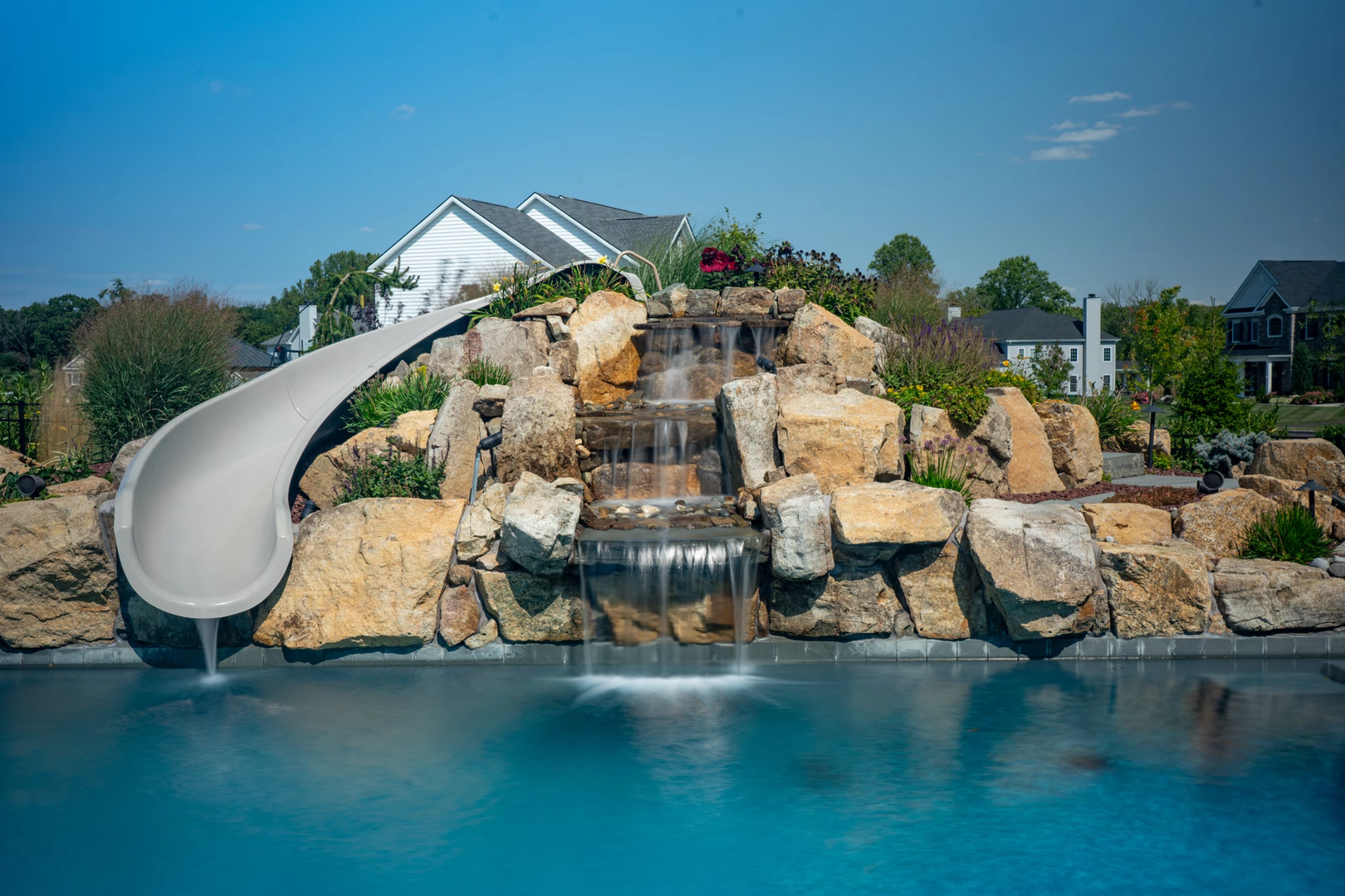 Natural stone boulder waterfall features cascading into a pool with lush landscaping