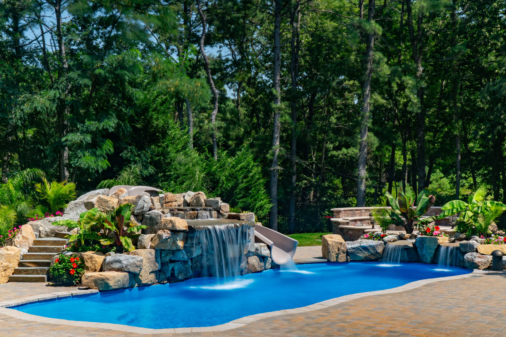 Cascading multi-tiered stone boulder waterfall flowing into a freeform pool with lush tropical plants