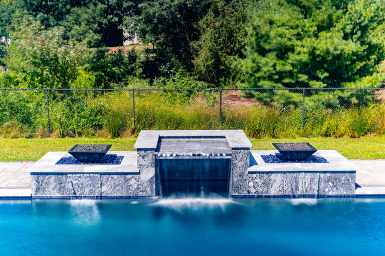 Stone waterfall cascading into a rectangular pool surrounded by lush green woodland landscaping