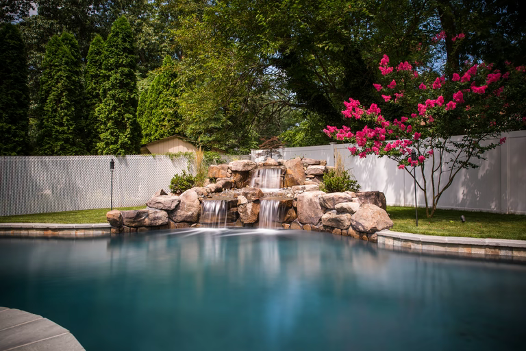 Natural stone boulder waterfall cascading into a pool beside vibrant pink flowering trees