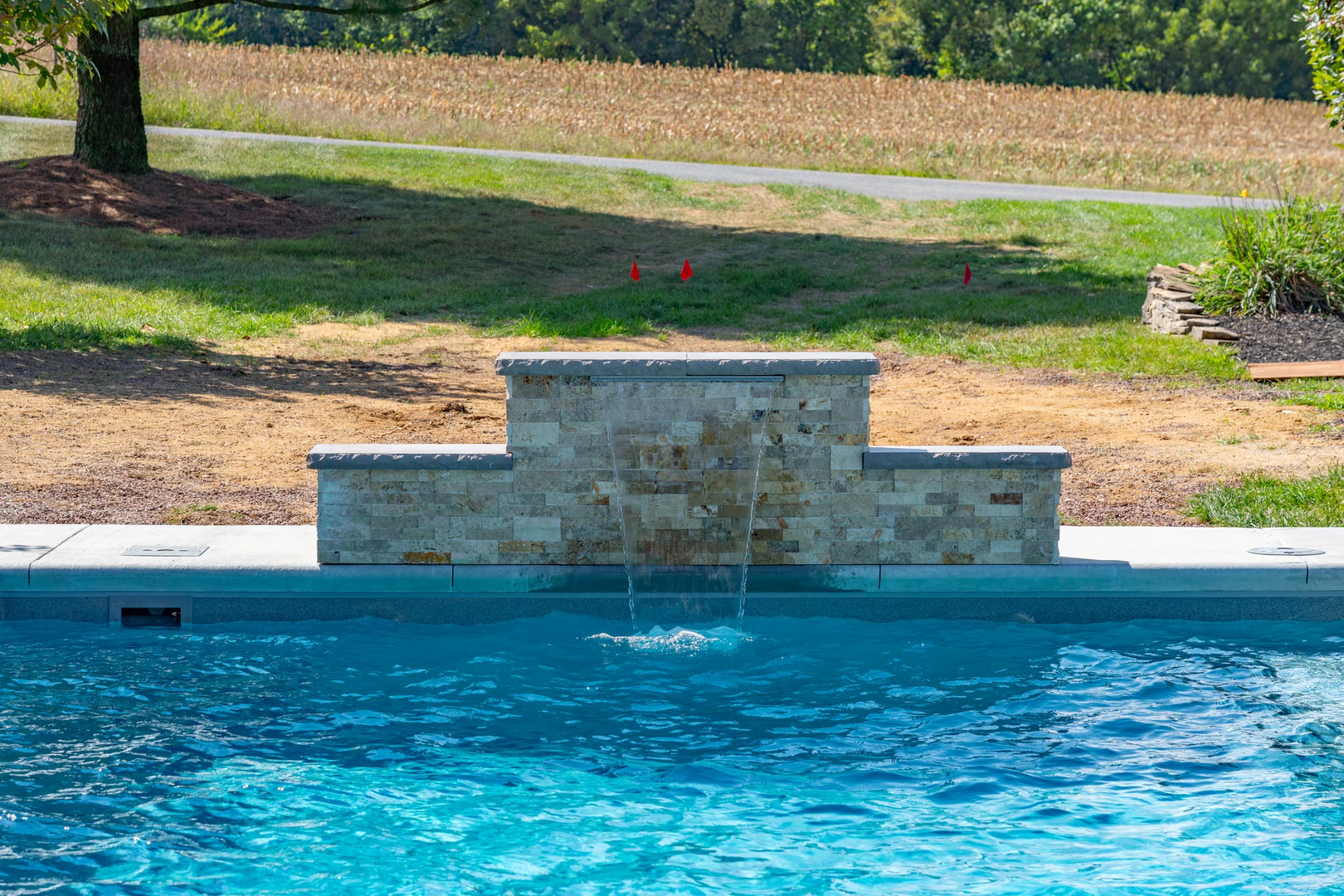 Three-tiered natural stone waterfall cascading into a pool with lush green lawn and trees