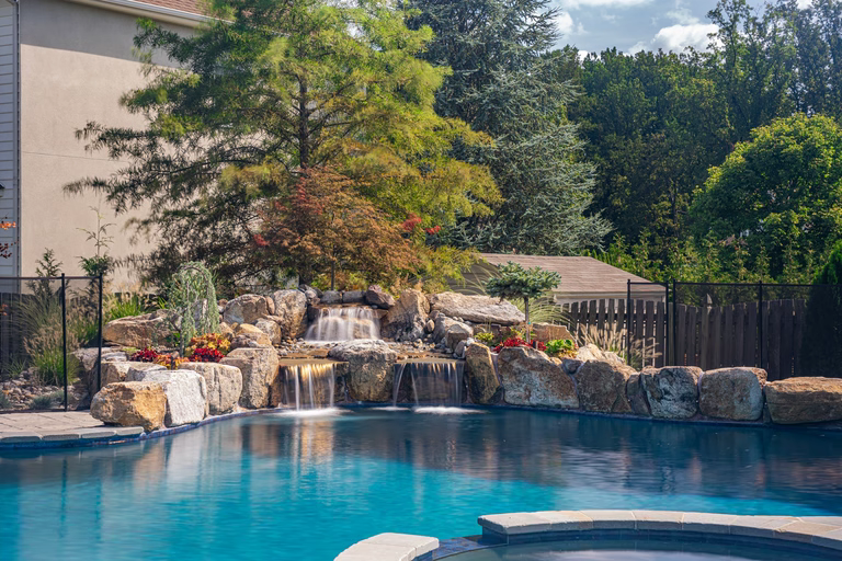 Natural stone boulder waterfall cascading into a pool surrounded by lush garden plants