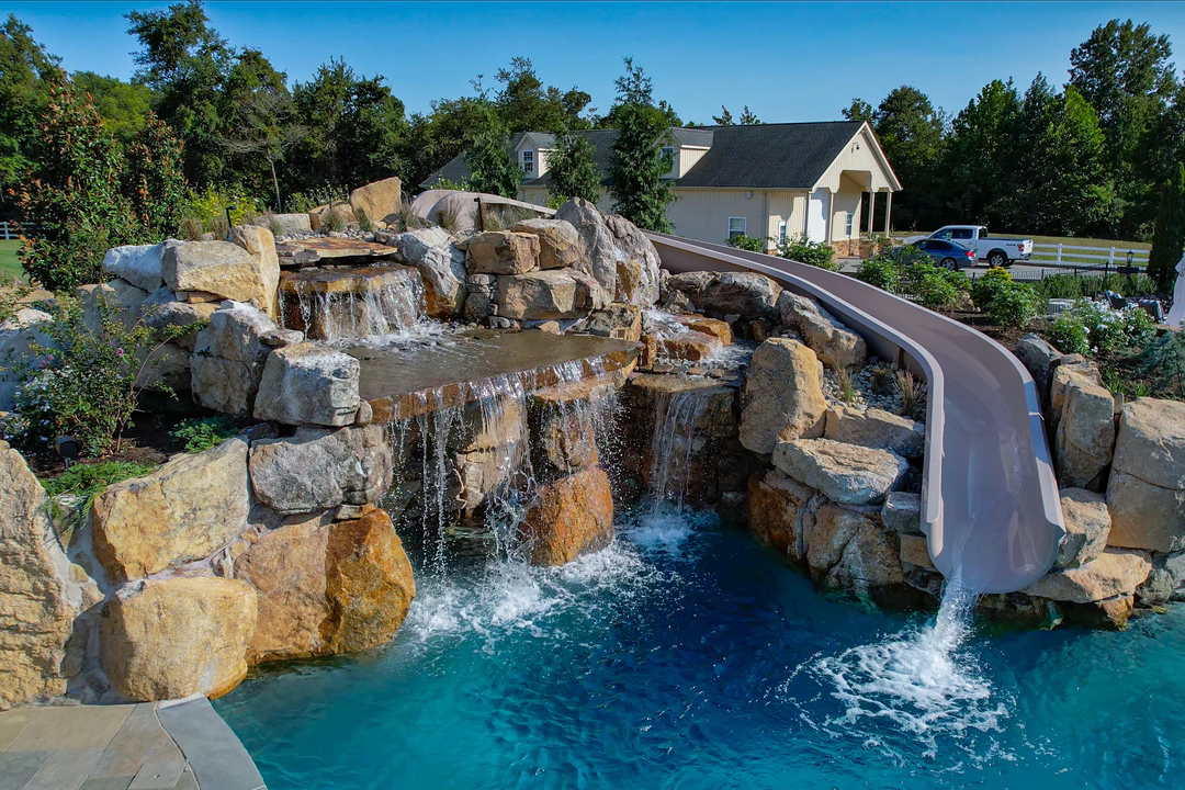Three-tiered natural stone boulder waterfall cascading into a pool surrounded by lush garden plants