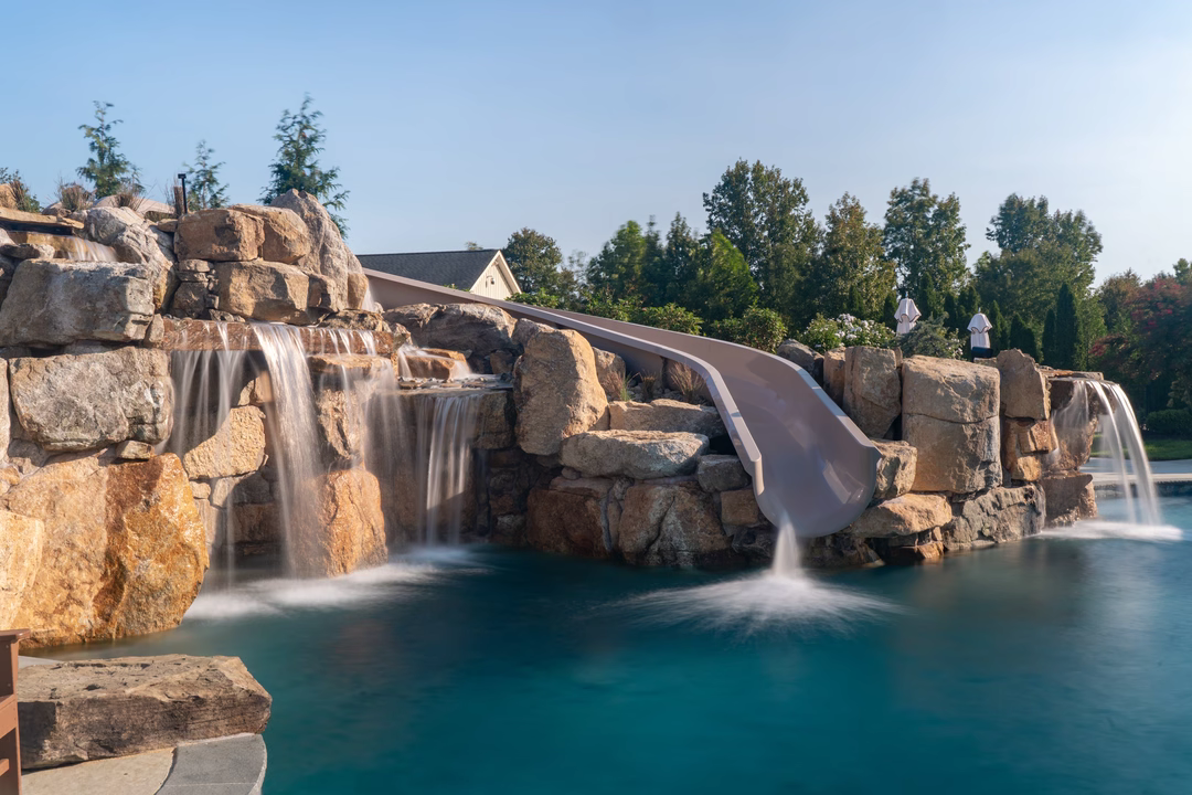 Multi-tiered natural stone boulder waterfalls cascading into a pool surrounded by lush green trees